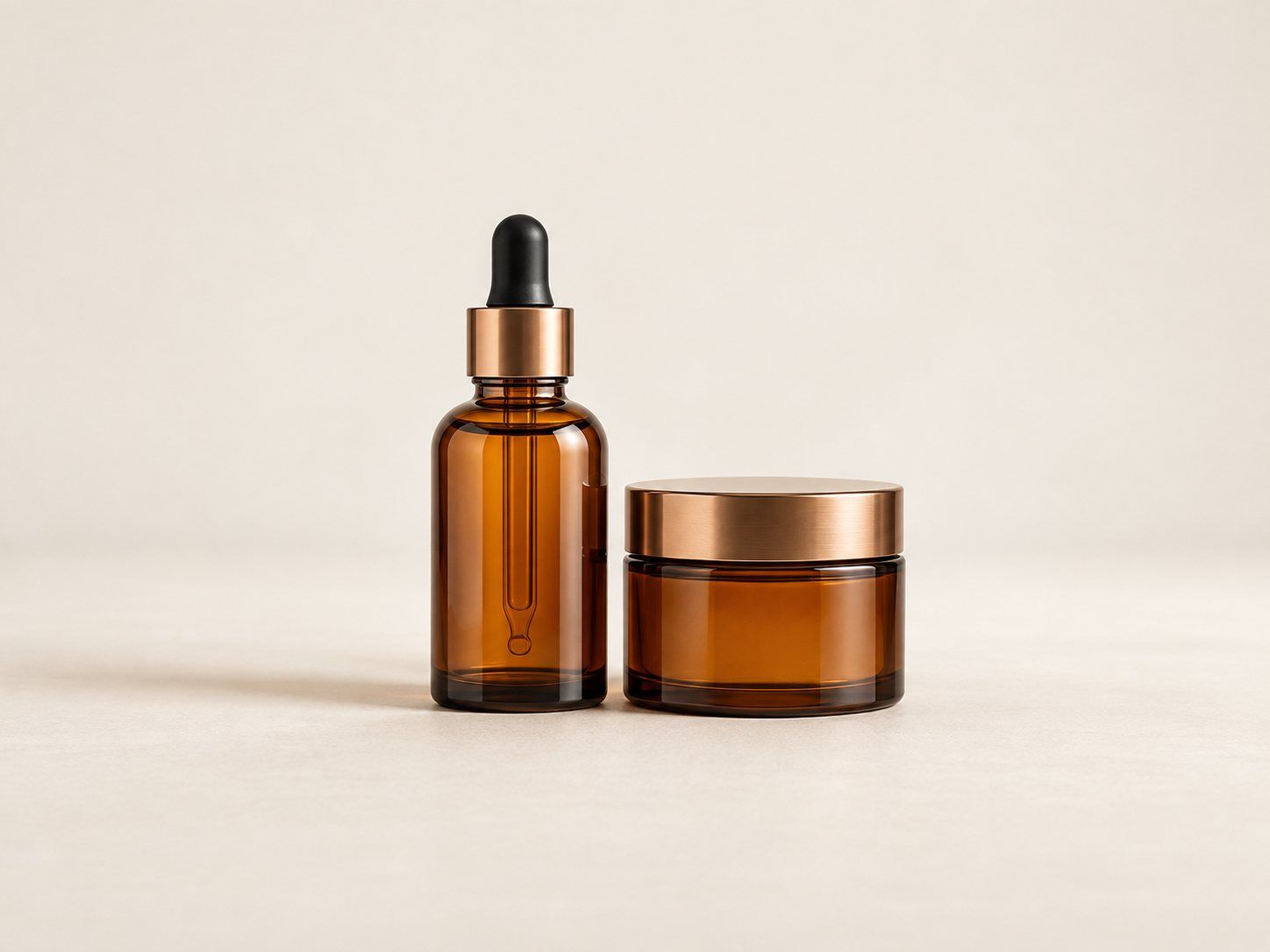 Unbranded amber glass bottles, a dropper bottle and a jar on a warm neutral surface