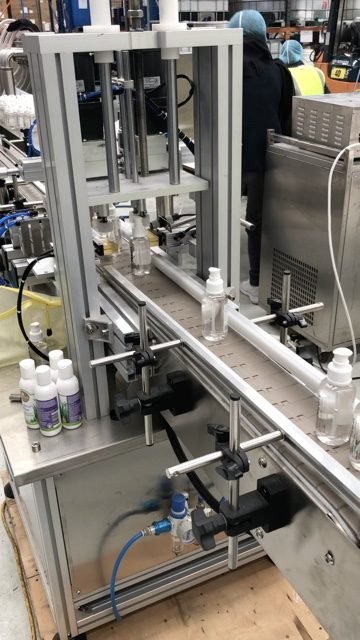 Clear bottles moving along a conveyor through a filling machine, with filled personal care bottles in the foreground